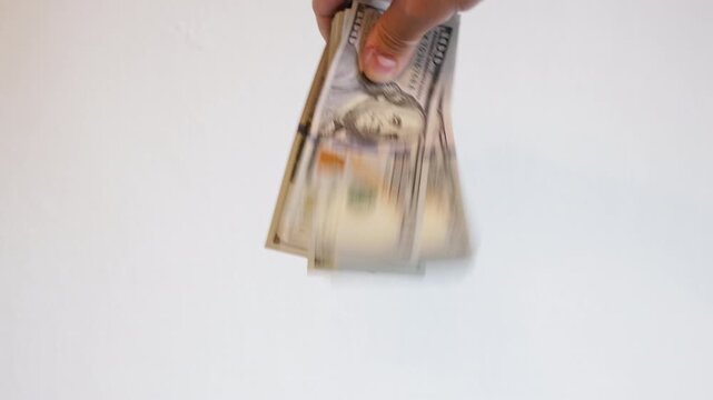 Adult hand holds and fans out a bundle of money against a plain background. Scene evokes feelings of wealth and opportunity in a financial context.