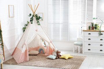 Toy wigwam with pillows, furniture and floral decor in room © New Africa