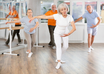 Obraz premium Happy aged woman in sportswear confidently leading ballet class with dancers following movements in modern dance studio