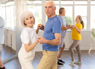 Fototapeta premium Group of happy elderly pensioners learning to dance latin dances in dance studio