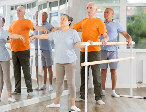 Active mature woman practicing second position holding by ballet barre during workout session in group