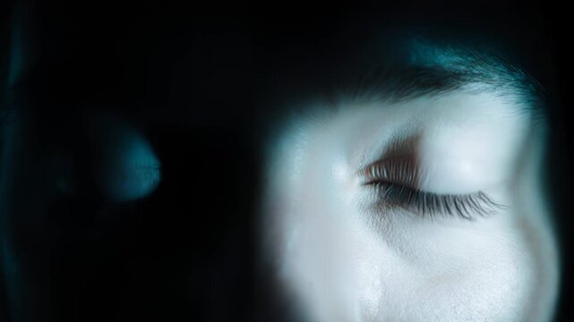 Close-up of a male face with striking blue eyes illuminated by soft light, showcasing the intricate details of the eyes and skin in a dark setting
