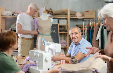 Obraz premium During sewing session for older adults, silver-haired man stitching at machine with smile, feeling at ease in mix of learning, socializing, and shared craft with group of likeminded people..