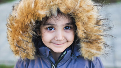 Smiling child in warm winter jacket with fur hood, looking at camera outdoors © Довидович Михаил