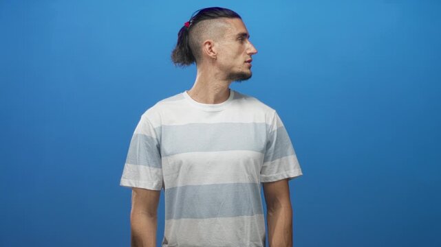 Man with visible face and forearms turns head to left in studio against blue seamless backdrop; quiet contemplation.
