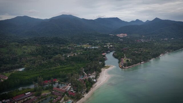 Aerial drone view of tropical beach, sea and Thai houses surrounded by lush forest. Scenic coastal landscape in Thailand with turquoise water and traditional buildings from above.