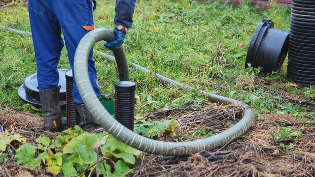 Worker performing septic tank maintenance, pumping waste using a large hose