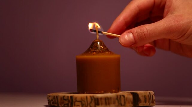 Woman hand lights a match the bees wax candle fire on wooden candlestick for mood, relaxation, meditation dark red background. Person lighting the decoration single candle flame