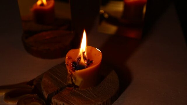 A brightly wind burning candle against a dark background near a mirror, the candle flame dripping melted wax onto the table. A magical witch ritual.