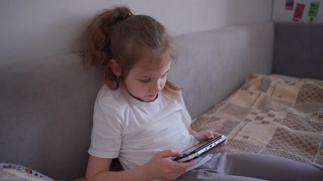 Girl Playing Game. Caucasian Girl Casually Enjoying Game On Handheld Device In Cozy Home Setting. Young Caucasian Woman Comfortably Engaging With Portable Gaming System While Leaning On Sofa