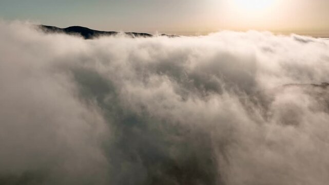The drone flies above clouds in Fanal forest located in Madeira, Portugal. View the inversion of clouds at sunrise with hills and trees below. Experience the natural beauty of the area. .Camera pan
