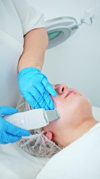 A professional esthetician cosmetologist performs ultrasonic facial cleansing peeling, deeply exfoliating the skin and cleaning pores.