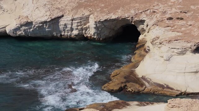 Aerial drone view of white limestone cliffs and turquoise water along the coast near Cape Greco, Ayia Napa, Cyprus, showcasing layered rock formations