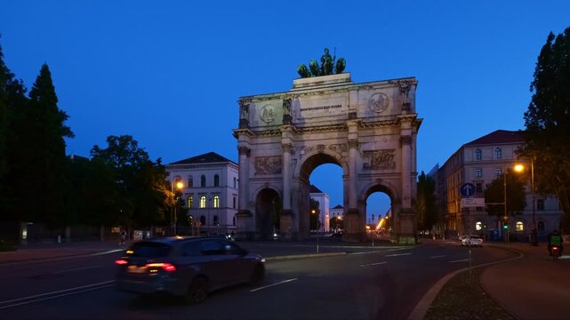 Night time lapse of traffic passing through the illuminated Siegestor (Victory Gate) in Munich, Bavaria, Germany, Germany at blue hour.