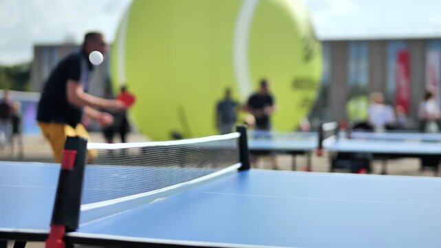 Ping pong game in public space with blurred players and giant tennis ball