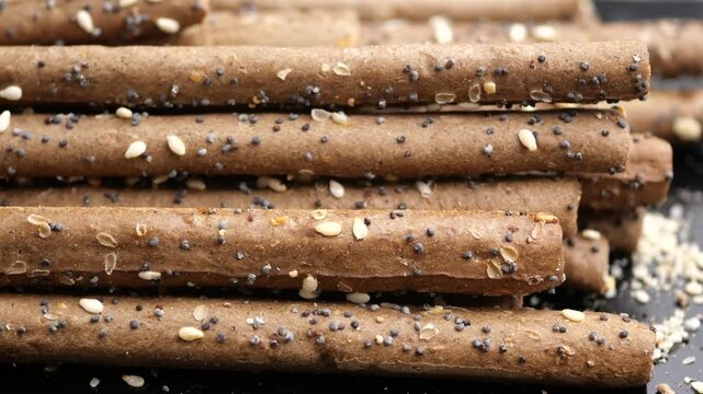 Close up motion footage of brown grissini breadsticks with poppy and sesame seeds.