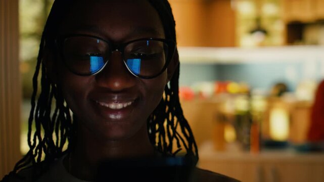 Black woman, doomscrolling, checking phone, texting at home, relaxing alone in the hallway with soft light indoors. Girl browsing the web on smartphone and enjoying peaceful domestic life.