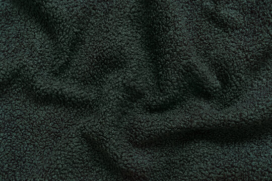 Detailed texture of dark green sherpa fleece fabric. Top view close-up of soft curly textile material for outerwear and interior design softly draped to create an abstract background