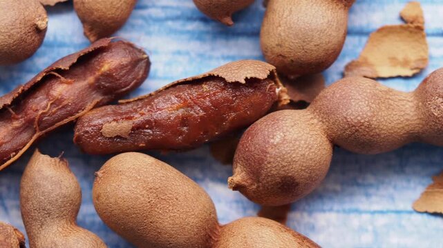 Top view of tamarind fruit pods and shell pieces on blue wooden table surface in close up.