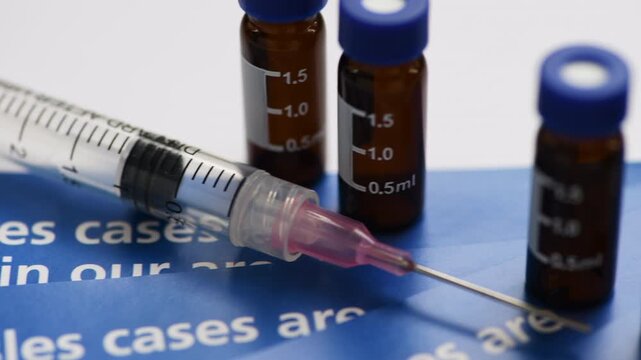A macro close up of information leaflets on a measles outbreak, a syringe needle and medical containers.