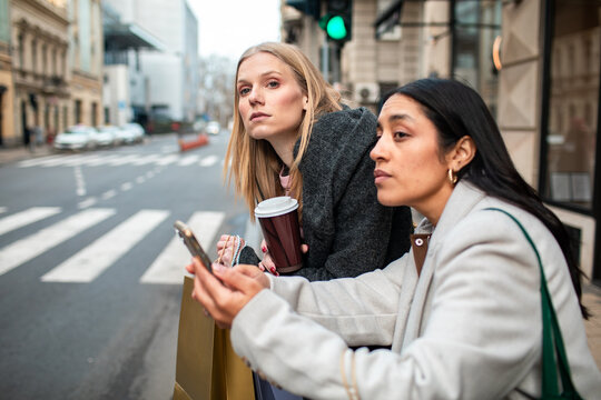Two women using smartphone while waiting at city crosswalk