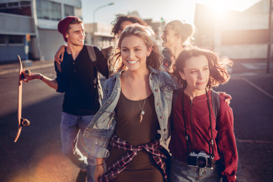 Group of happy friends walking through city at sunset