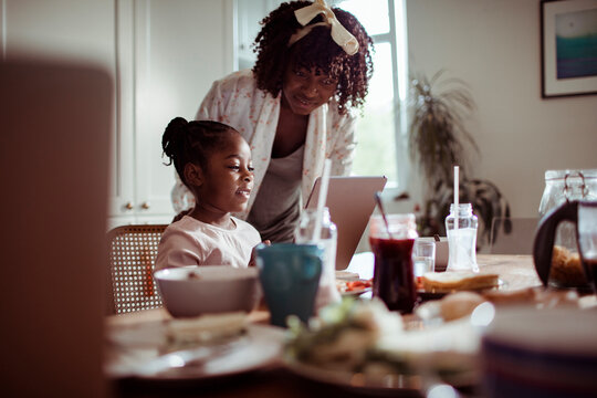 Mother helping daughter with tablet at kitchen table