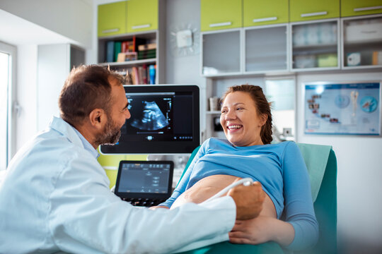 Doctor performing prenatal ultrasound with happy pregnant woman in clinic