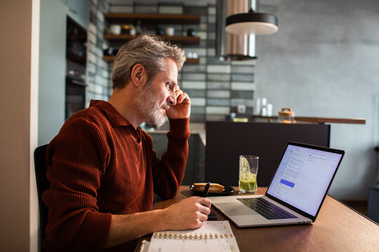 Middle-aged man checking email on laptop at kitchen table