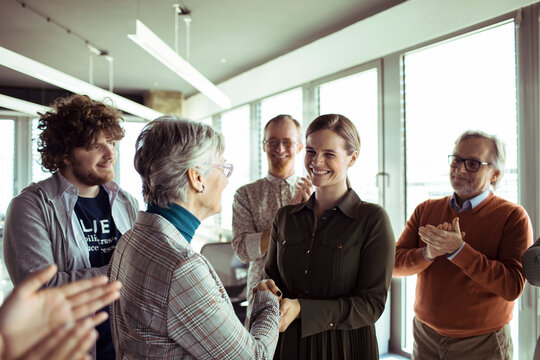 Colleagues applauding promotion handshake in modern office