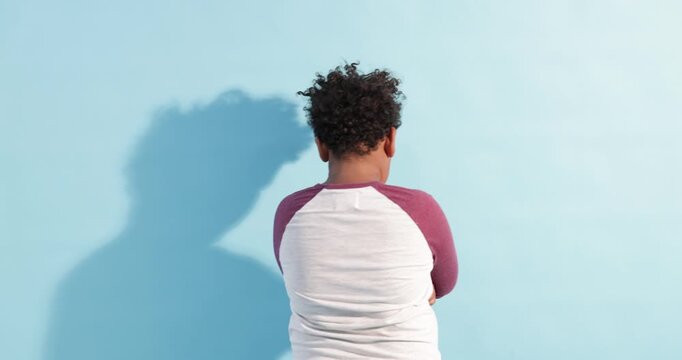 Resentful little boy with crossed arms on light blue background