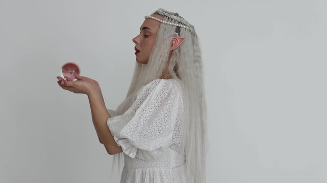 Beautiful girl dressed as elf with glass ball on white background