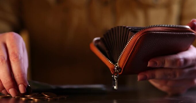 Woman putting dollar banknotes and coins into wallet at wooden table, closeup