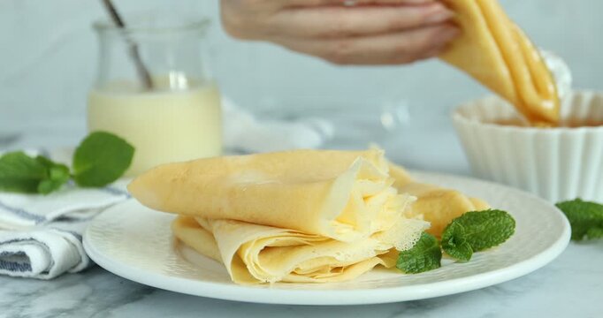 Woman dipping tasty crepe into honey at white marble table, closeup