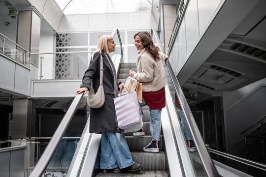 Women friends talking on escalator with shopping bags