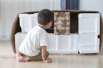 A Thai child exploring and examining a cardboard and foam box fort, showcasing curiosity and imaginative play. © bonnontawat