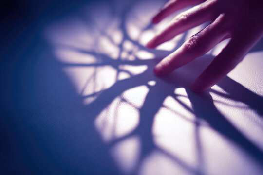 Raynaud syndrome causes blue fingers with dramatic shadow patterns on white surface, highlighting emotional impact of this vascular condition in close up hand image