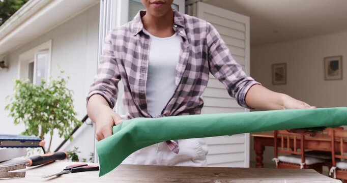 African American woman seeing loose green fabric, lifting frame, pulling taut for stapling on porch