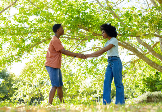 African American couple holding hands under large leafy tree in sunlit park wearing casual clothes