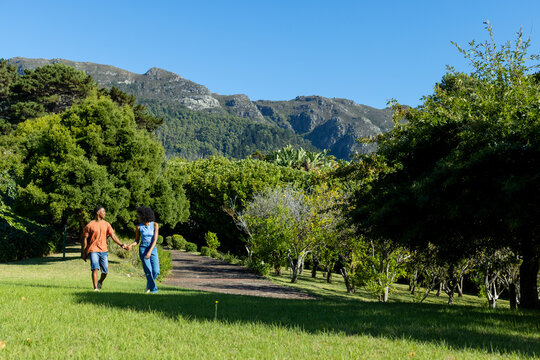 African American couple holding hands walking on park lawn beside dirt path with yellow stake