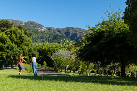 Couple holding hands walking across mown grass at park toward dirt path and ridge, copy space