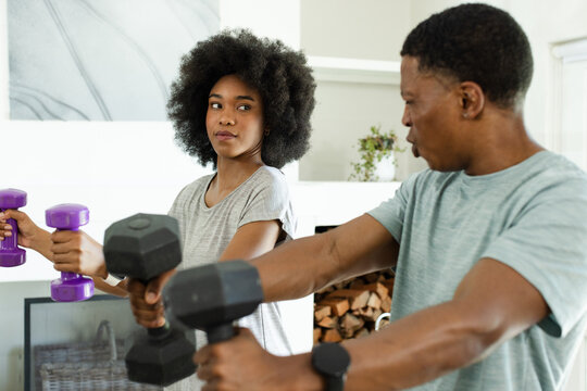 African American couple lifting purple and black dumbbells, doing front raises in living room