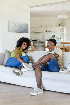African American couple chatting on light-colored sofa in open-plan living room near kitchen