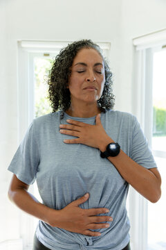 Woman posing in room with tall windows, greenery, wearing knotted gray tee, black smartwatch