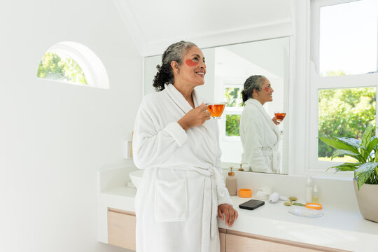 Morning light streaming window causing woman holding amber cup wearing patches for skincare routine