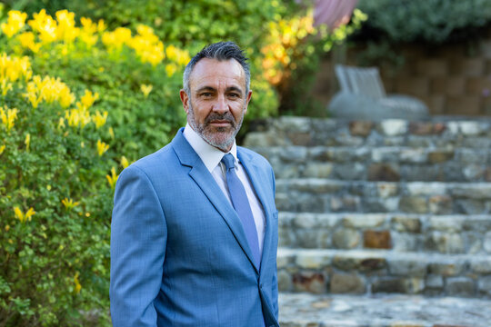 Vertical video: Standing man in blue tailored suit facing camera in garden, posing for portrait