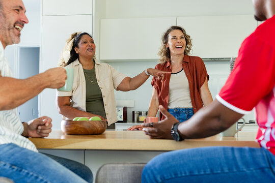 Diverse friends in casual clothing laughing around kitchen island with wooden bowl of apples