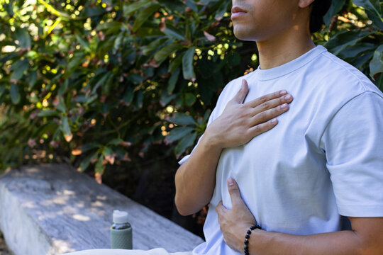 Asian man sitting on stone bench, holding reusable bottle and showing beaded bracelet, copy space