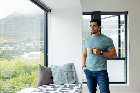 Man standing in sitting nook holding ceramic mug wearing smartwatch near window view, copy space