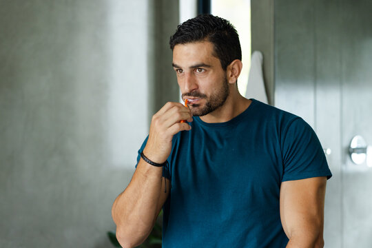 Man standing and flossing teeth with orange interdental pick in bathroom wearing dark teal t-shirt